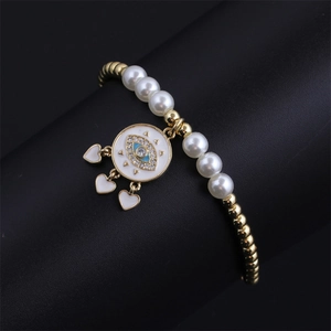 Detail of gold beaded bracelet with evil eye pendant and white heart charms on stand