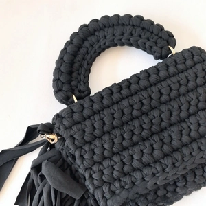 Close-up of handmade crochet bag detail showing textured knit, fringe, and gold ring