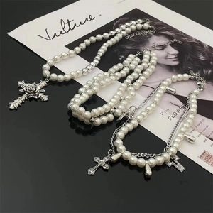 Detail of layered pearl necklaces with silver cross and rose pendants on black surface