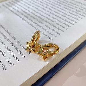 Close-up of gold star charms on hoop earrings placed on a vintage book page