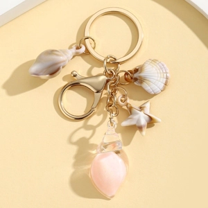 Golden keychain with pink conch shell and starfish charms on a beige tray