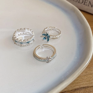 Close-up of a three-piece silver flower ring set with blue enamel and sparkling zircons