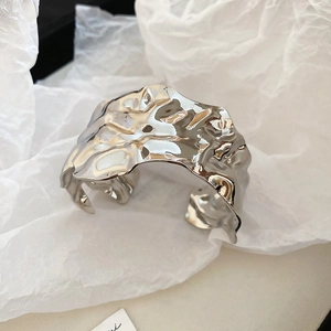 Close-up of a wide silver cuff with a liquid metal wrinkled texture and minimalist style