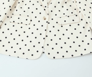 Détails du blazer à pois avec deux poches à rabat et bouton ambre sur tissu beige