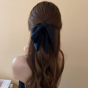 Close-up of a large black silk bow hair claw clip with shimmering rhinestones on long hair