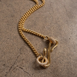 Zircon snake pendant necklace with cuban chain on stone background, gold finish