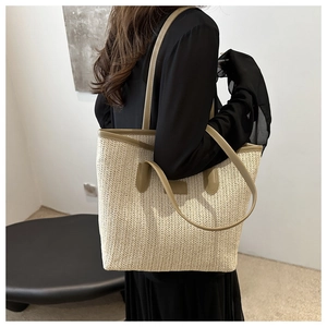 Detail of a large woven straw tote bag with khaki leather handles and herringbone texture