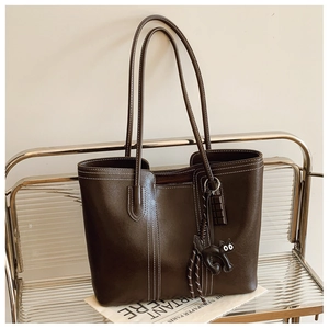 Close-up of brown leather tote bag with cat charm on transparent display stand