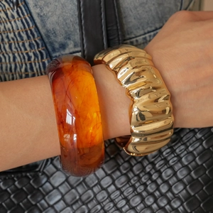 Detail of a wide gold wavy metal bangle paired with an amber resin bracelet on a wrist