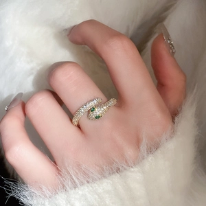 Close-up of gold snake ring with green zircon eyes worn on finger over soft white fur