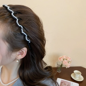 Detail showing wavy black headband with white pearls worn by a model in a cozy setting