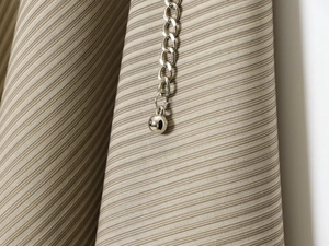 Détail d'une chaîne en métal argenté avec pendentif sphérique sur tissu beige à rayures