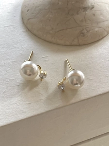 Close-up of elegant gold pearl earrings with cubic zirconia on a marble base