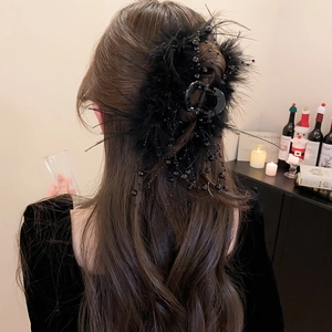 Detail of luxury black feather hair claw clip with glossy beads worn on wavy hair