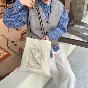 Detailed shot of white lace tote bag with purple floral pocket and black handles on shoulder