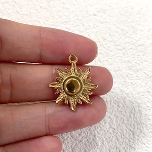 Detail of a small gold sun-shaped pendant charm held by hand over textured fabric