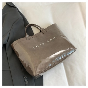 Detail of a brown glossy tote bag with bold TOTE BAG text on a stylish fabric setup