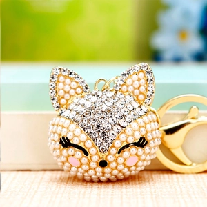 Macro shot of diamond-encrusted fox car keychain with white pearls and gold metal plating