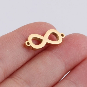 Macro detail of a small golden infinity symbol connector held on a fingertip for DIY jewelry