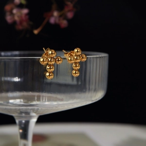 Macro shot of gold stainless steel cross stud earrings on a textured glass rim