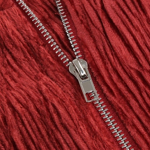 Close-up of a silver metal zipper on dark red corduroy fabric with sharp ribbed texture