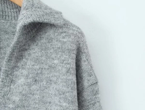 Gros plan d'un pull en maille grise montrant la texture douce et les détails du col