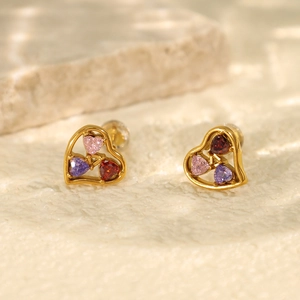 Golden heart earrings with pink purple and red zircon stones on a white stone background