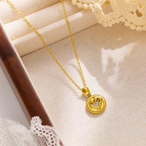 Close-up of gold sweater chain with rhinestone heart disc pendant on wood box