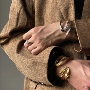 Artistic twisted metal open cuff bracelet and silver ring set on a model in brown suit