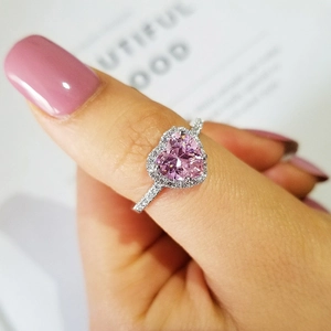 Close-up of a pink heart-shaped gemstone ring with halo diamonds on a hand
