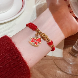 Gros plan d'un bracelet de perles rouges avec charm cheval doré et calligraphie