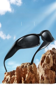 Matte black oversized sports sunglasses displayed on rocks under a bright blue sky