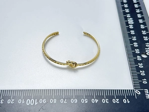 Gros plan d'un bracelet jonc à nœud en acier doré 18K avec règle de mesure graduée