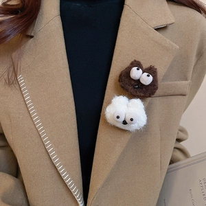 Close-up of cute plush big-eyed monster brooches in brown and white on a camel blazer