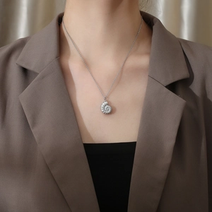 Close-up of a silver conch shell pendant necklace worn over a professional brown blazer