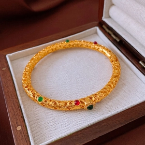 Macro shot of 24K gold plated bangle with intricate filigree and red green gemstones
