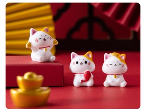 Detailed close-up of three lucky cat resin figurines with golden fish and festive decor