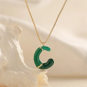 Primo piano della collana dorata con pendente a lettera C in smalto verde elegante