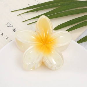Macro shot of white and yellow acrylic frangipani hair claw clip on a white plate