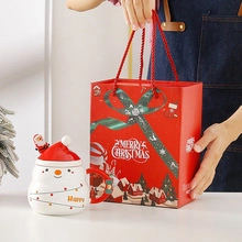 Christmas snowman ceramic mug with red hat lid and spoon in a festive holiday gift bag