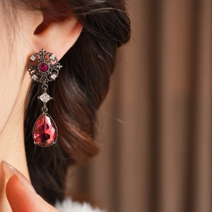 Détails de boucles d'oreilles vintage avec cristaux bordeaux et accents floraux argentés