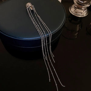 Detail of silver long tassel chain ear cuff with glossy metallic beads on dark background