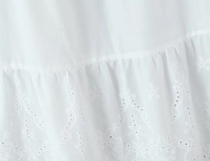 Detailed close-up of white cotton fabric with hollow embroidery and scalloped edges