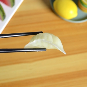 Miniature realistic dumpling model being held by black chopsticks on a wooden table