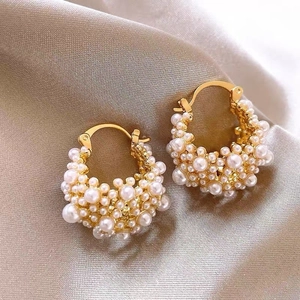 Detailed shot of gold hoop earrings with white pearls on elegant champagne silk fabric