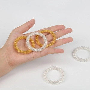 Close-up of gold and silver spring massage rings held by hand on white background
