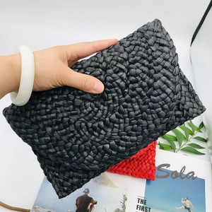 Handmade woven corn husk clutch bag in black and red held with elegant magazine props