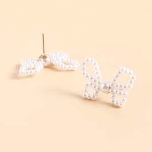 Close-up of pearl bow earrings with golden metal details on a neutral background