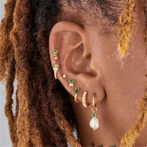 Close-up of gold earrings set with emerald green stones, zircons and baroque pearls