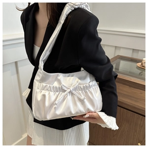Detail of white pleated satin shoulder bag with bow decoration on black blazer